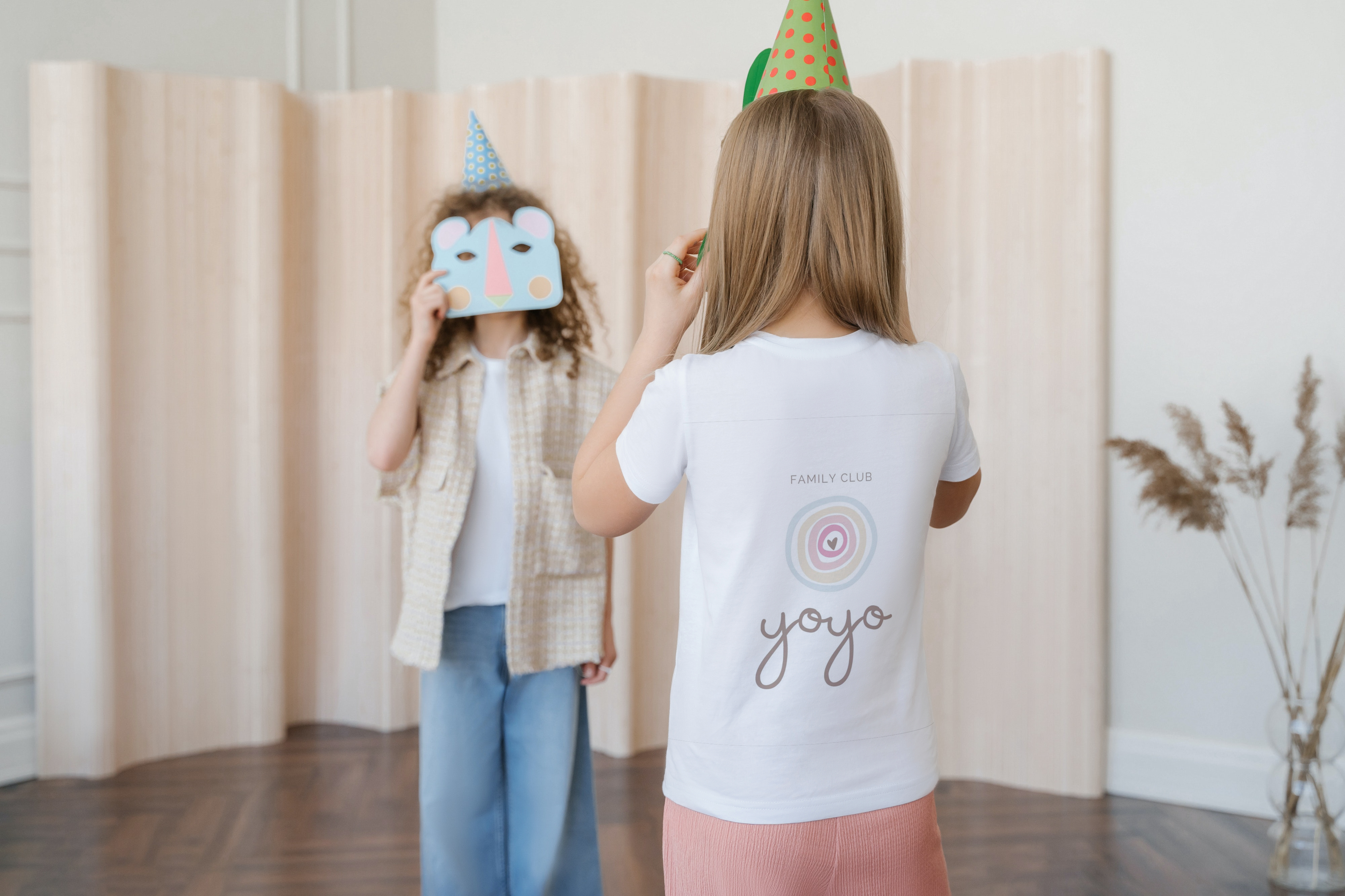 Bambine con cappellini da festa, una con maschera azzurra, l'altra di spalle con maglietta bianca «Family Club yoyo